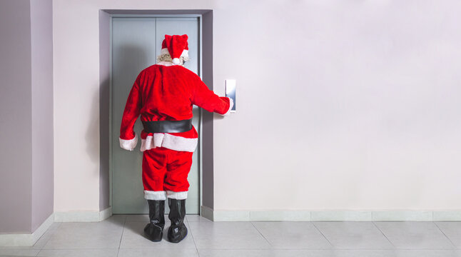 Man in Santa Claus costume calls elevator in building at Christmas