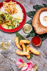 Exotic summer dinner with two glasses of sparkling wine, rice with curry sauce, prawns fried in noodles and a beautiful serving on natural gray textured stone