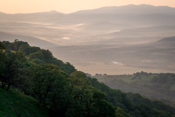 Obraz premium Early morning just after sunrise. Silhouettes of mountains in the morning haze, tree branch in the foreground. Alpine summer landscape.