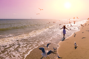 Seascape. Sunrise over the sea with a beautiful sky. Woman on the beach. Summer. Young happy woman with hands in the air walks along the seashore. Seagulls fly over the beach