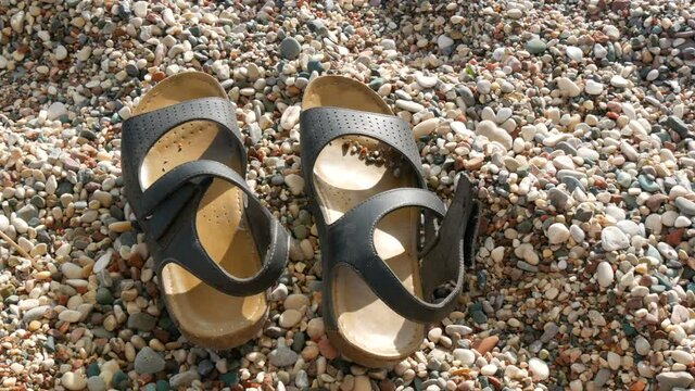 Lonely leather sandals on the beach of rocky pebble sand on the seashore in summer, vacation concept.