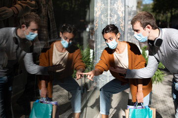 Shopping during Coronavirus pandemic concept. A young couple wearing face masks in front of a shop window.