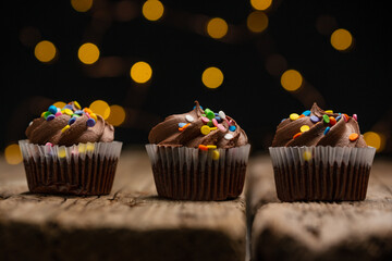 Tasty chocolate cupcakes on rustic wooden table with yellow lights on black background. Sweet dessert. Bakery concept. Delicious food.