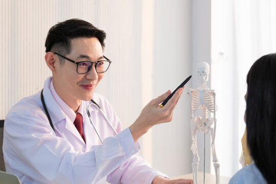 Neurosurgeon pointing at lumbar vertebrae model in medical office explaining information to patients. Physiotherapist pointing at bone model explaining to patient. 