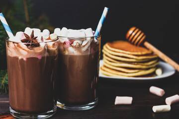 Hot chocolate with marshmallows and straws on a background of pancakes with honey