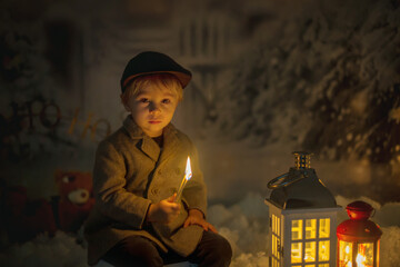 Little boy, looking at flame from match, sitting in the snow