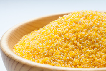 Corn grits in a wooden bowl isolated on white background. Close-up.