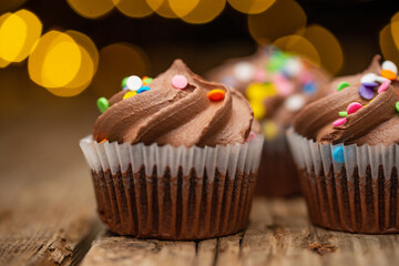 Chocolate cupcakes on rustic wooden table with yellow lights on black background. Sweet dessert. Bakery concept. Delicious food.