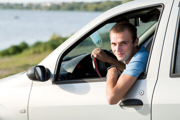 A young man looks out of the window of his car.