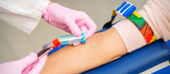 Nurse on pink gloves takes blood sample from vein from female patient in medical laboratory
