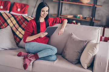 Obraz premium Photo of lovely young lady sit couch hold tablet wear red sweater jeans socks in decorated living room indoors