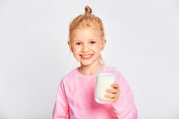 Cute little girl holding a large glass of milk. Kid 4-5 year old posing in studio on gray background