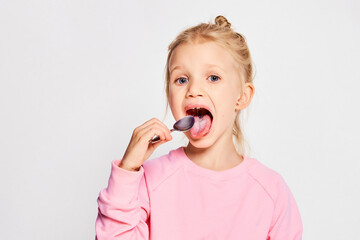 Cute little girl eating tasty yogurt on gray background. 4-5 year old kid posing in studio in a...
