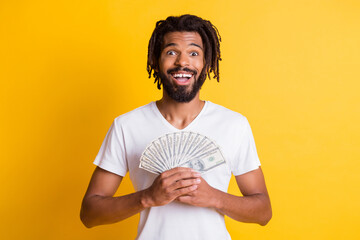 Photo of young black guy hold dollar money cash fan wear white t-shirt isolated yellow color...