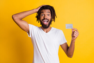 Photo of black guy hand head hold credit card open mouth wear white t-shirt isolated yellow color...