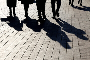 Silhouettes and shadows of people on the city street. Crowd walking down on sidewalk, concept of crime, society or population - obrazy, fototapety, plakaty