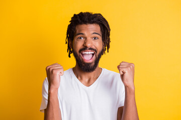 Photo of overjoyed dark skin guy raise fists celebrate victory wear casual t-shirt isolated yellow color background