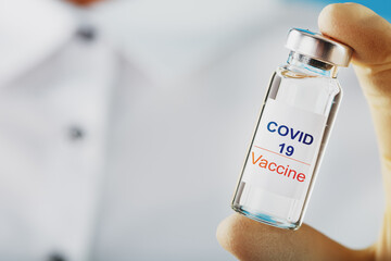 An ampoule with the inscription COVID-19 vaccine in the hands of a doctor-scientist in rubber gloves with a vaccine.