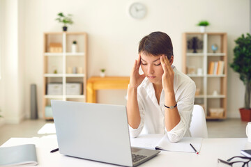 Fototapeta na wymiar Tired woman with bad headache or blurry vision massaging temples sitting at desk with laptop