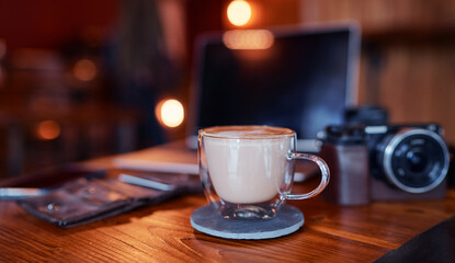 Traveler's breakfast. Cup of cappuccino on wooden table with laptop and photocamera.
