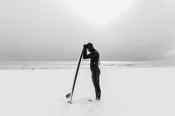 Snowy winter and surfer with surfboard. Winter beach and surfer in wetsuit.