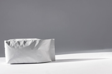 Blank white foil pouch bag on grey background in minimal style with natural hard shadows....