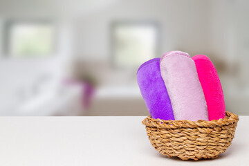 Basket with three colorful terry towels or cosmetic for body care on a white table over blurred bath background with copy space. For your product display montage.