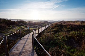 Fototapeta premium Wooden pedestrian walkway through Sintra-Cascais natural park. Wild sandy landscape, with part of Cresmina Dunes. Beautiful scenery in Portugal.