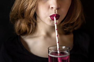 A young girl with bright pink lipstick drinks a cocktail from a glass from a paper tube. The concept of ecology and environmental protection.