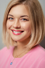 Fototapeta premium Portrait of happy blonde woman smiling and looking at camera on grey background.