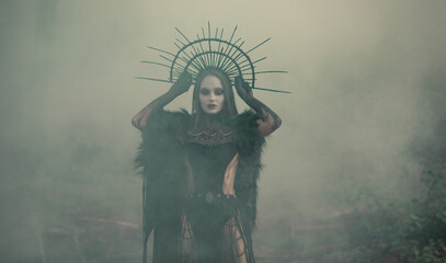 Woman in image of witch stands in dark and foggy forest.