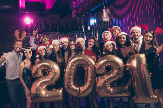 Photo portrait of people with 2021 balloons showing v-signs wearing goofy glasses santa claus caps reindeer headwear at party