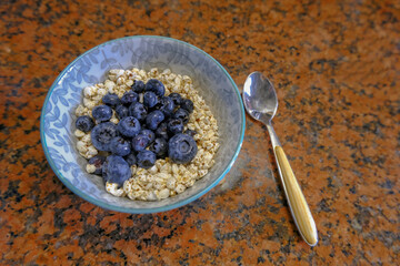 bowl of rice cereal and blueberries, spoon on marble table close-up. Top view. Healthy breakfast, lifestyle.