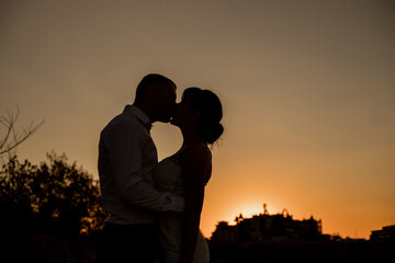 A black silhouette of a kissing couple against the background of the sunset. Shadows form the heart.