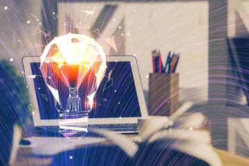 Computer on desktop in office with bulb icon hologram. Double exposure. Concept of idea.