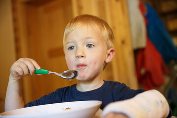 Little boy with a broken wrist eating at the table. Boy with a plaster on his arm.