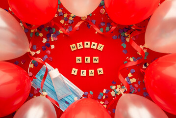 Happy new year written in English with wooden letters and decorated with face mask, gel, balloons colored and confetti. Covid concept.