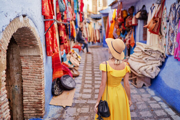 Colorful traveling by Morocco. Young woman in yellow dress walking in  medina of  blue city Chefchaouen.