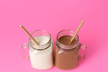 Glass jars with flavoured milkshakes against pink background