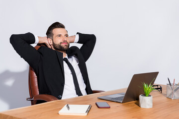 Photo of handsome cheerful business guy notebook table having break hands behind head look dreamy empty space wear black blazer shirt costume sit chair isolated grey background