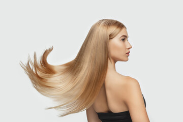 Wave. Beautiful model with long smooth, flying blonde hair on white studio background. Young caucasian model with well-kept skin and hair blowing on air. Concept of salon care, beauty, fashion.