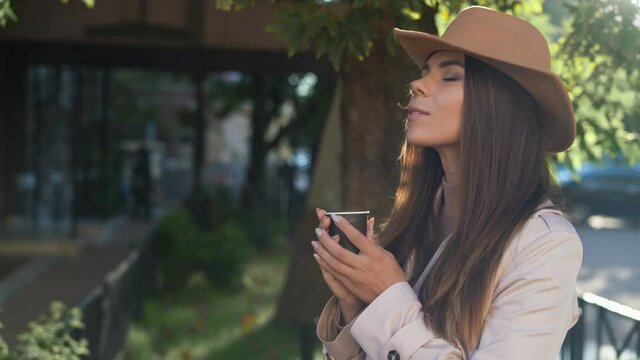 young beautiful woman in a felt hat stands on the street. Inhale the aroma of morning coffee, disposable paper cup. High quality 4k footageyoung beautiful woman in a felt hat stands on the street. Inh