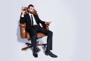 Full length photo of handsome business guy sit chair hold pack money dollars drink luxury expensive scotch ready pay wear black blazer pants tie shirt shoes suit isolated grey background