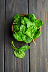 Fresh spinach leaves in wooden bowl on dark rustic background. Healthy vegan food concept. Eco-conscious vegan lifstyle. Top view.