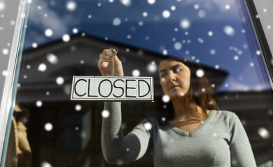 small business, people and service concept - young woman hanging banner with closed word on door or...