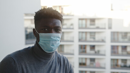 Fototapeta na wymiar Black man with medical mask on the balcony Looking to the camera. Quarantine and mental health problems. High quality photo