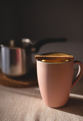 Pink mug with curcuma latte and cinnamon stick. Vertical photo