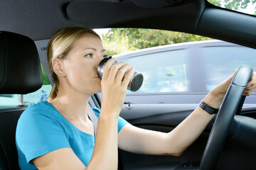 Fototapeta na wymiar Frau fährt Auto und trinkt Kaffee oder Tee aus Thermobescher und ist dabei abgelenkt vom Verkehr auf der Straße