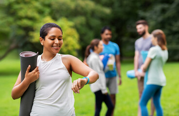 sport and healthy lifestyle concept - african american woman with mat looking at fitness tracker...