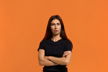 Obraz premium Are you serious. Portrait of attractive funny emotional caucasian woman in black t-shirt looking at camera, keeping arms crossed and open mouth, feeling shocked. Isolated over an orange wall